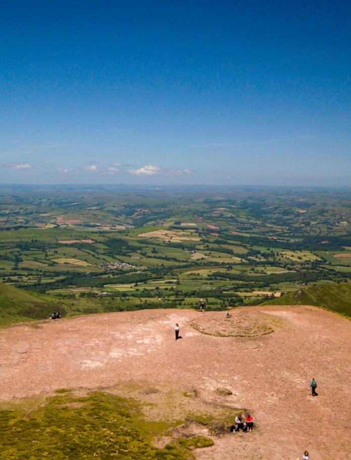 Aerial view of the green plains below from the top of Pen y Fan with blue skies.