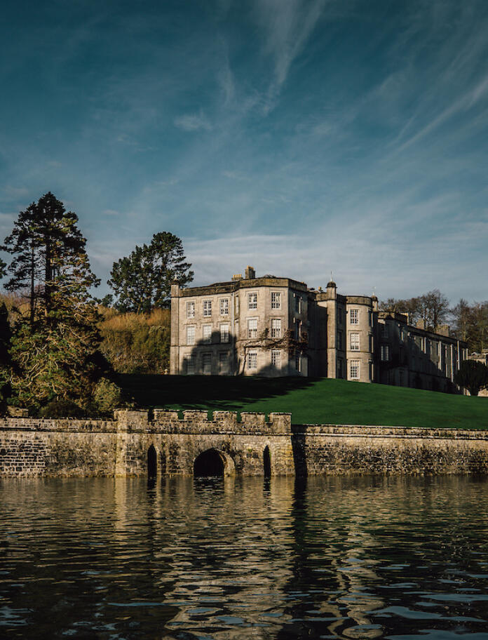 On the water looking at the Plas Newydd building with blue sky behind and green trees surrounding.