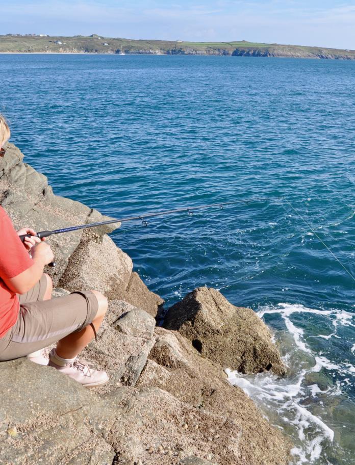A woman fishing off rocks into the sea.