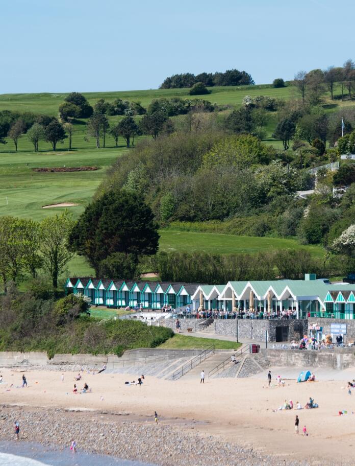View from sea towards sandy beach with green beach huts.