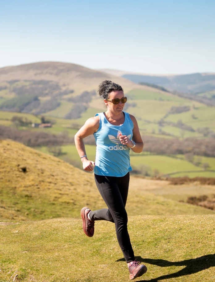 Woman running across moorland with hills in the background.