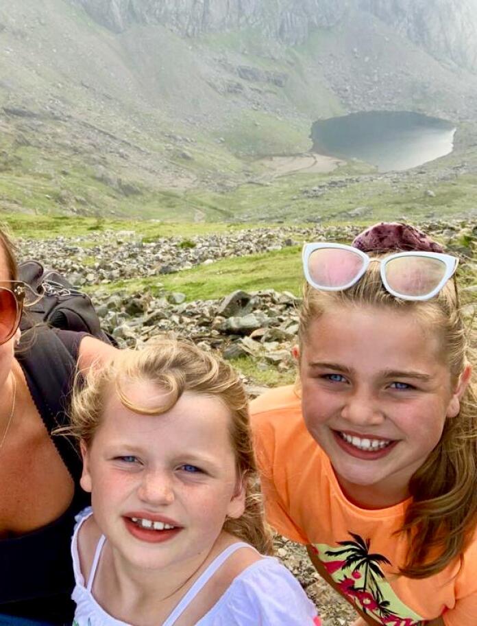 Eine Familie (Vater, Mutter und zwei Töchter) lächelt auf dem Gipfel des Snowdon (Yr Wyddfa).