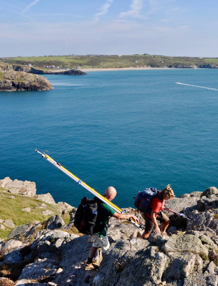 Two people with fishing rods walking on a cliff.