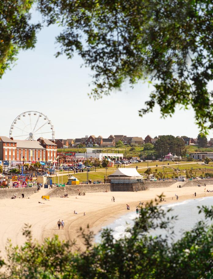 Beach and funfair viewed from distance through trees.