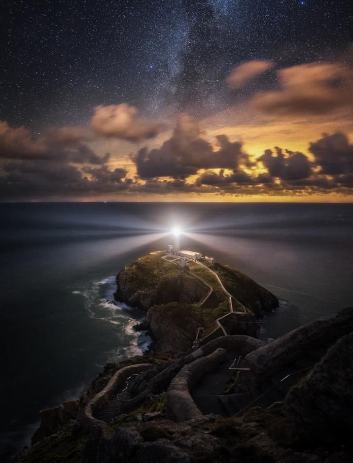 The light shining bright from South Stack lighthouse with the sunset highlighting clouds in the darkening sky.