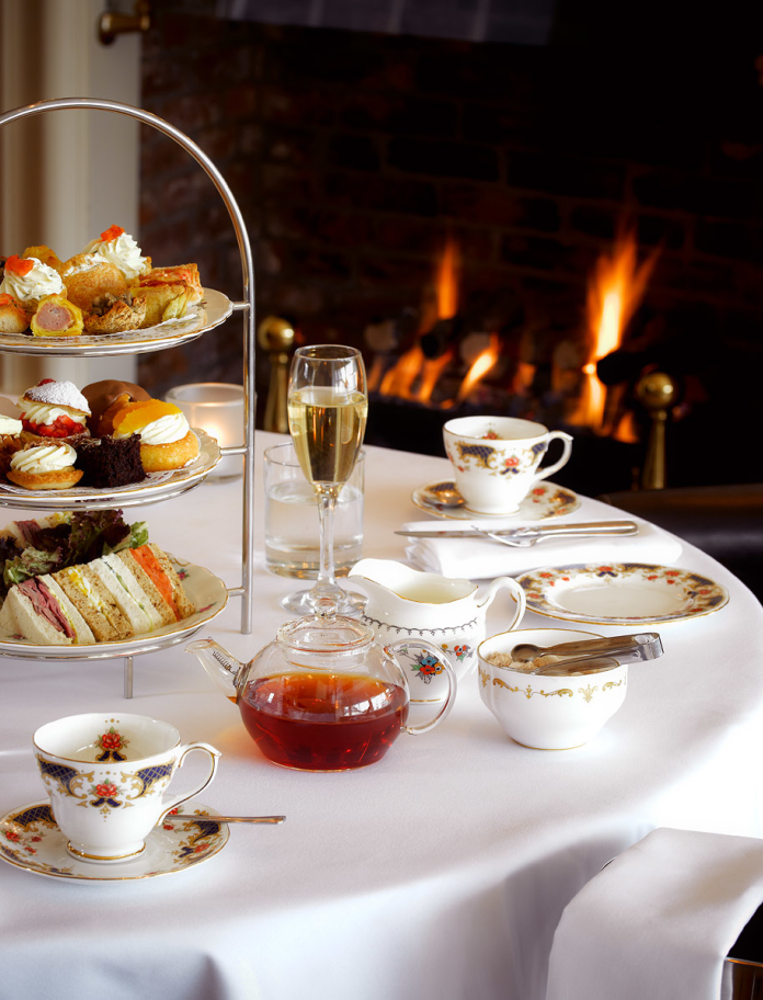 Table with afternoon tea, champagne bottle and fire in background.