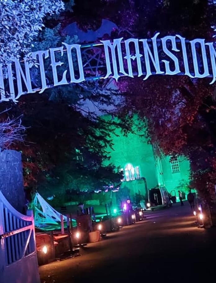 nightshot with lights and sign 'Haunted Mansion' above gate.