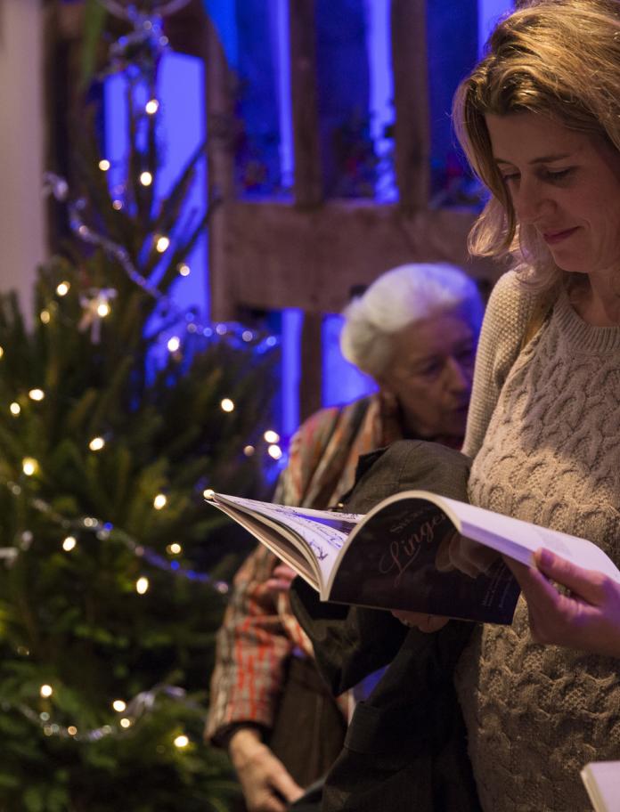 Eine Person steht lesend mit einem Buch neben einem Weihnachtsbaum.