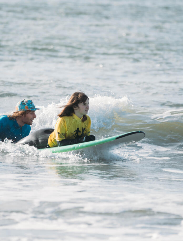 A young lady being helped to use a surfboard. 