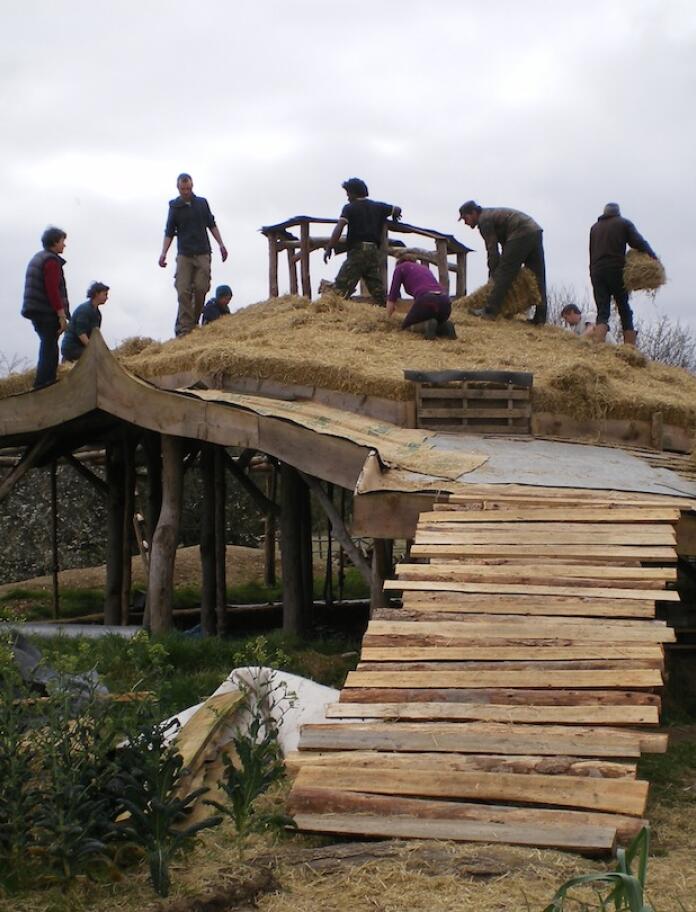 people laying a strawbale roof on a building.