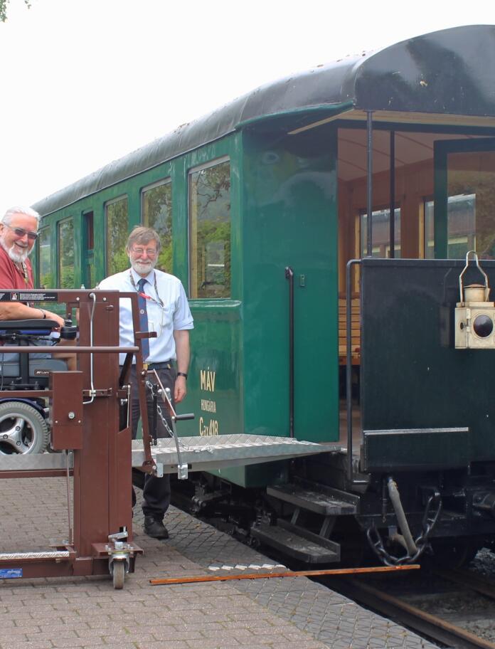 man on wheelchair lift with another man standing steam train.