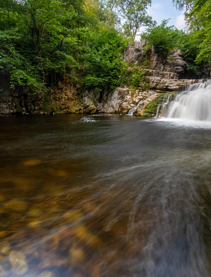 Ein Wasserfall, der über Felsen in ein großes Becken fließt.