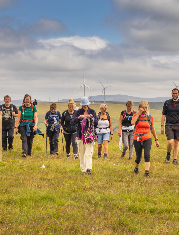 Eine Gruppe von Wanderern auf einem Hügel mit Windkraftanlagen im Hintergrund.