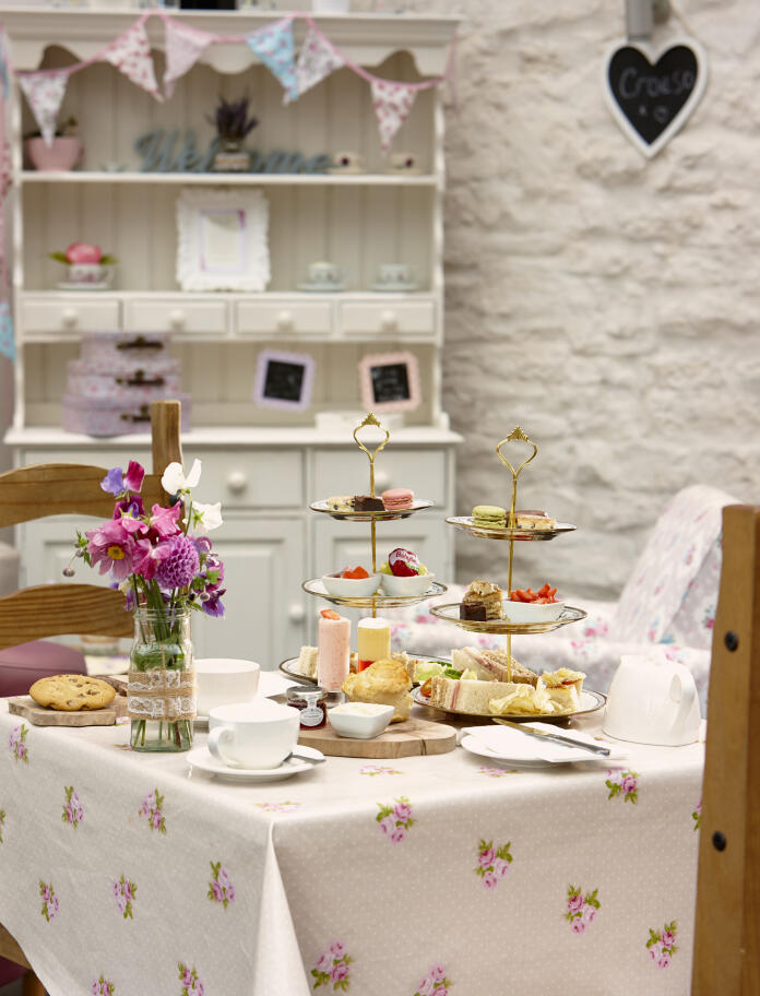 A tiered cake stand with a variety of sandwiches and cakes on a table laid for afternoon tea.