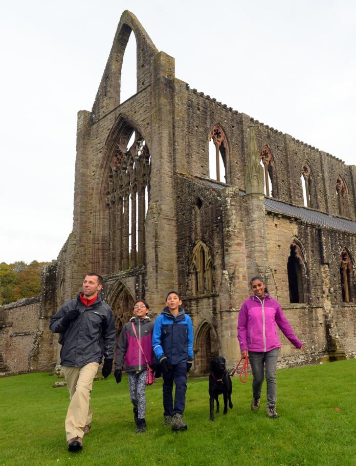 A group of people with a dog walking round a ruined abbey.