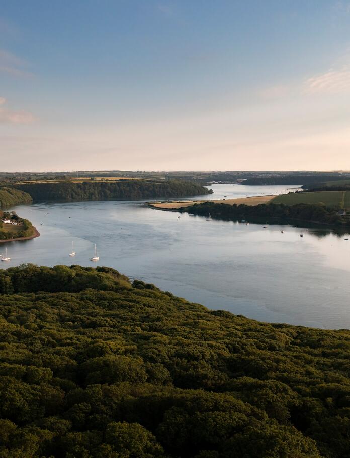 Aerial view of an estuary surrounded by green woodland.