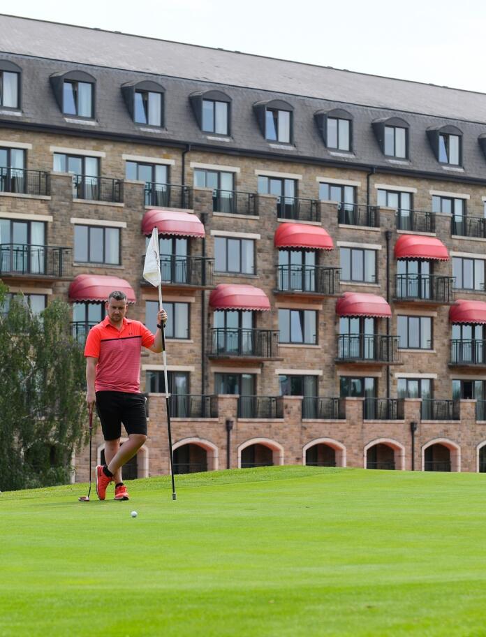 Three men playing golf in front of a hotel