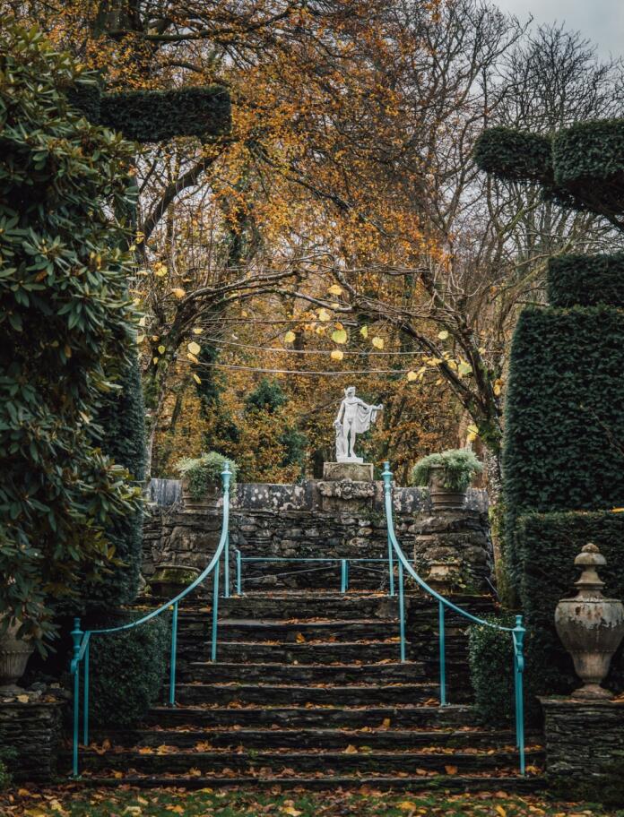 Garden steps between manicured hedges,  leading up to a statue.