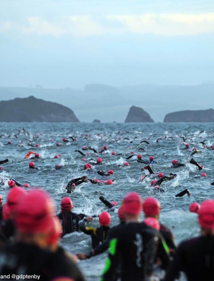 competitive swimmers in sea, plus swimmers with red caps lined up to go into the sea.