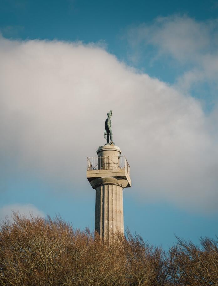 A tall pale stone column with a viewing platform and statue at the top.