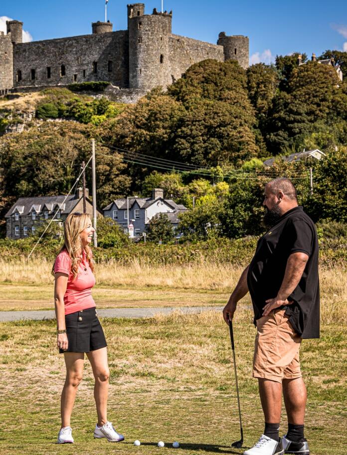 Two golfers chatting on a golf course underneath a huge castle.