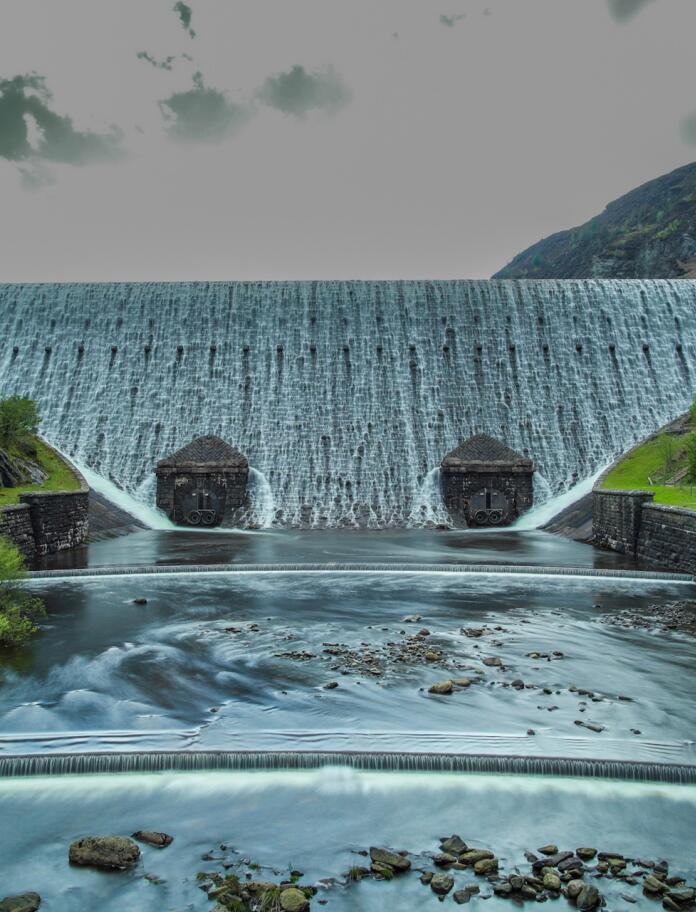 Ein Staudamm mit überfließendem Wasser und einem Bach im Vordergrund.