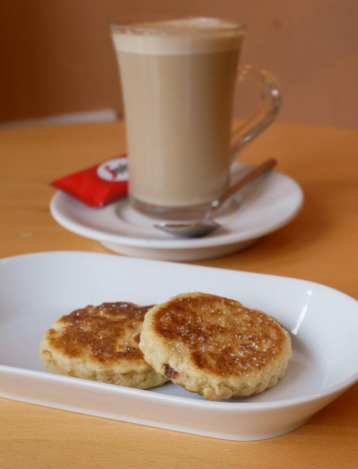 Zwei Welsh Cakes auf einem weißen Teller, daneben ein Milchkaffee.