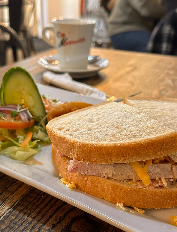 A doorstep of a ham and cheese sandwich on white bread, with a side salad.