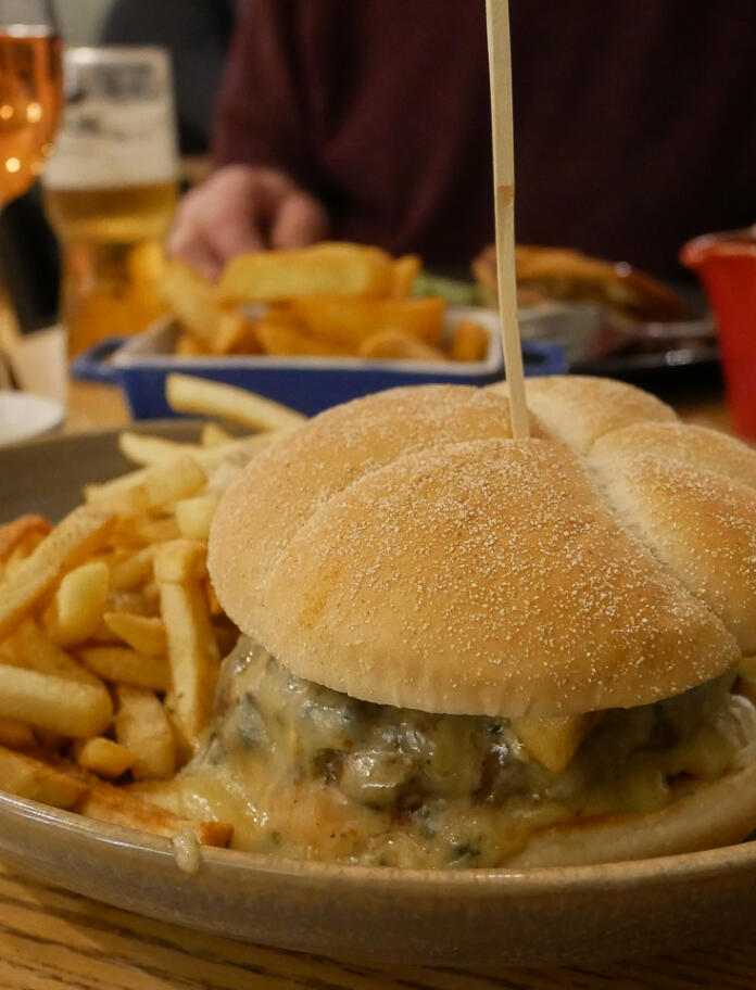A large burger in a bun, with melting cheese oozing out and fries on the side.