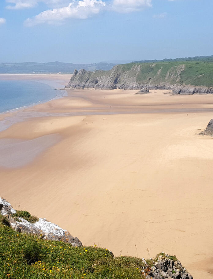 A wide sandy beach in between high cliffs. 