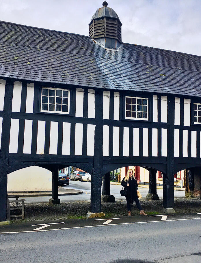 A black and white timbered long building with arches under the first floor.