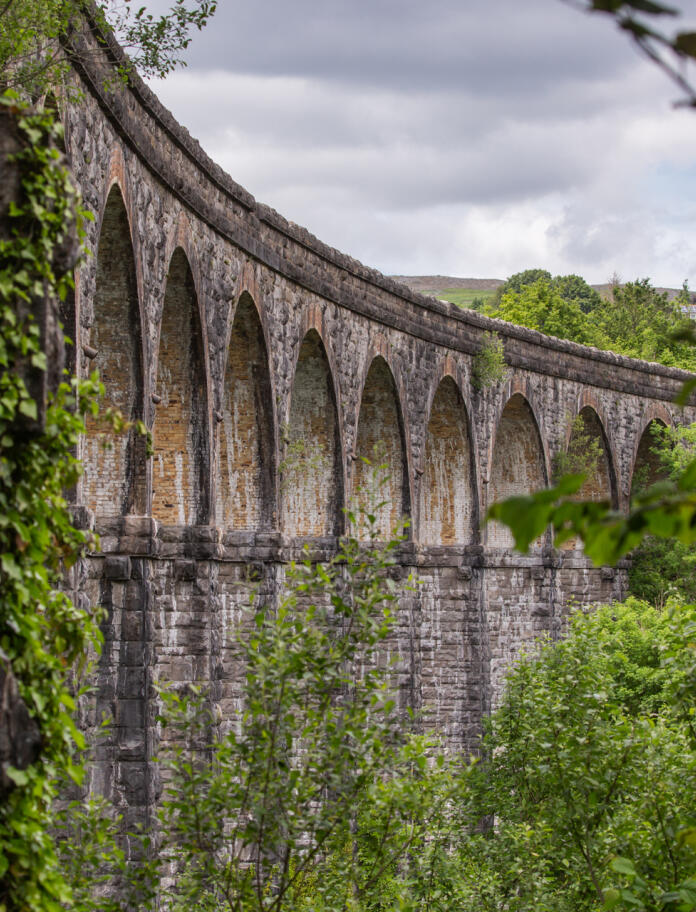 A viaduct with 13 curved stone arches surrounded by green trees.