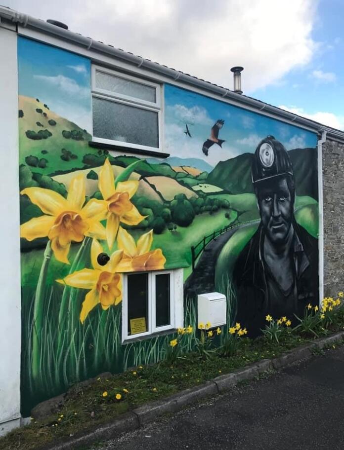 Exterior shot of mural on the back of the cottage depicting a miner, daffodils and rolling green hills.