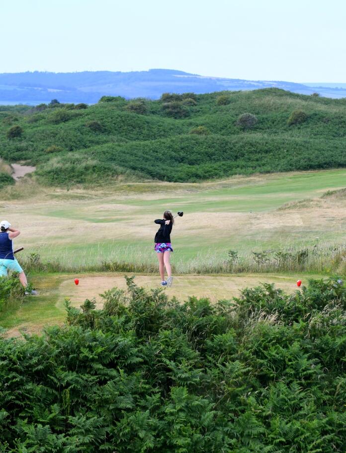 A female golfer taking a shot on a golf course surrounded by grassy dunes.