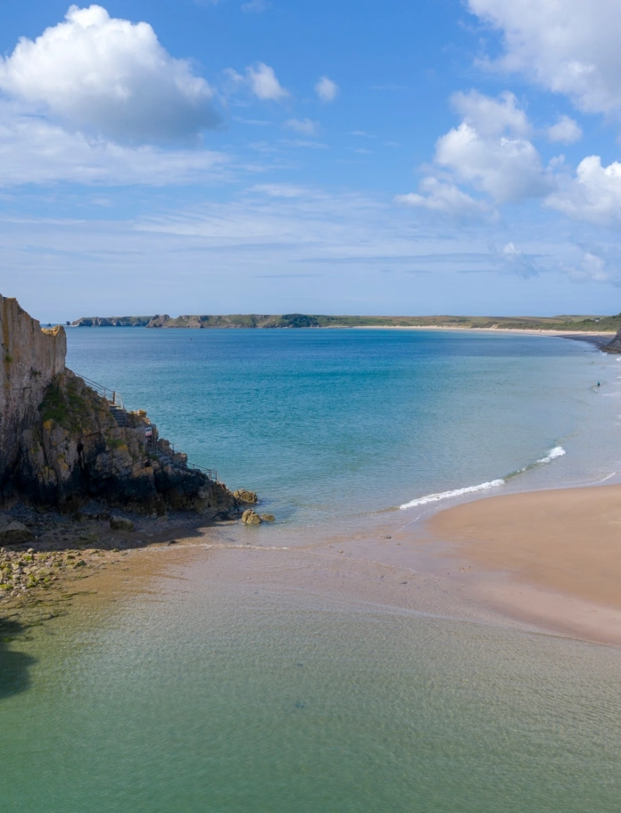 Picture of a sandy beach with rocks and houses in the background.