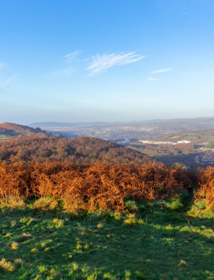 Ausblick von einem Berg auf eine Stadt und grüne Hügel im Hintergrund.
