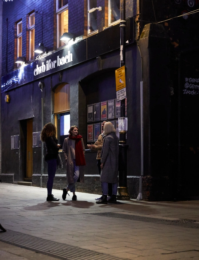 People talking standing outside the front of a building at night.