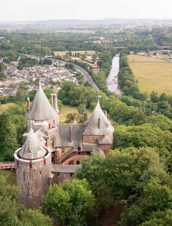 A fairytale-style castle overlooking a river and a road, towards a city.