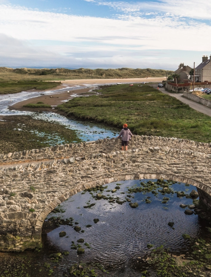 A person on a stone bridge looking towards a beach.