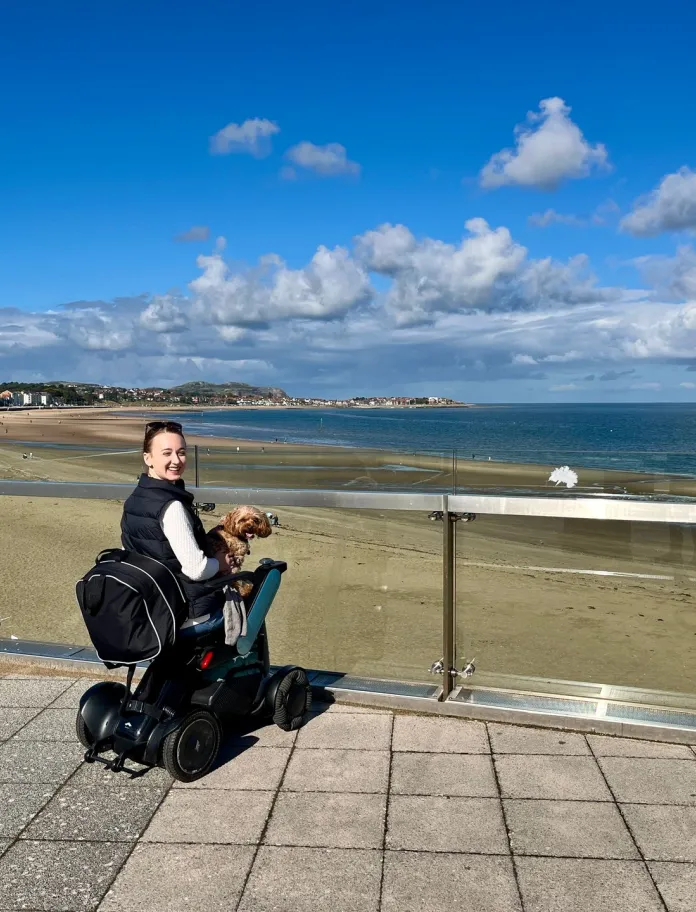 woman on the promenade in power-chair and cuddling dog in the sunshine.