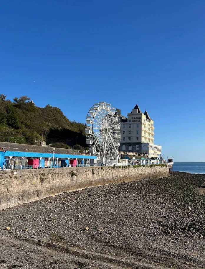 pebbly beach and sea with big wheel and hotel in background.