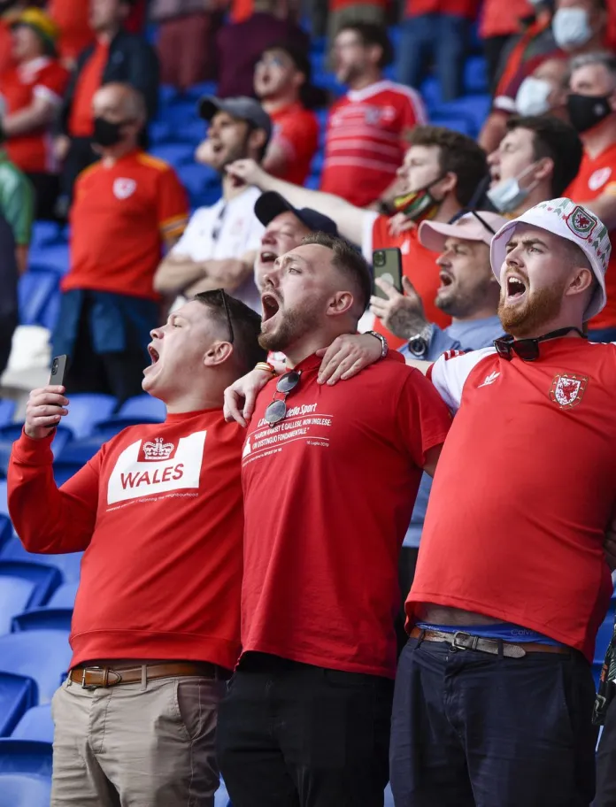Crowds of football fans in a stadium wearing Welsh football tops.