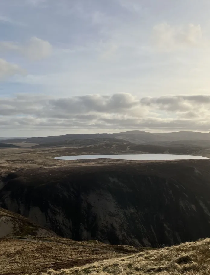 Mountain lake on a high plateau at Glaslyn Nature Reserve, surrounded by rolling Cambrian Mountains beneath a cloudy sky.
