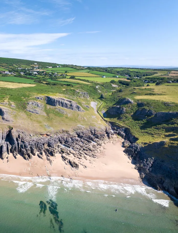 Aerial view of a small sandy cove with clear sea, surrounded by cliffs.