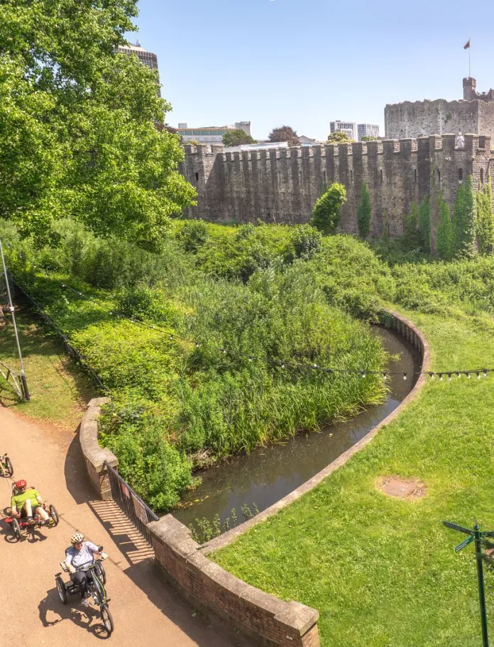 A group of cyclists using adapted bikes in a park with a castle. 