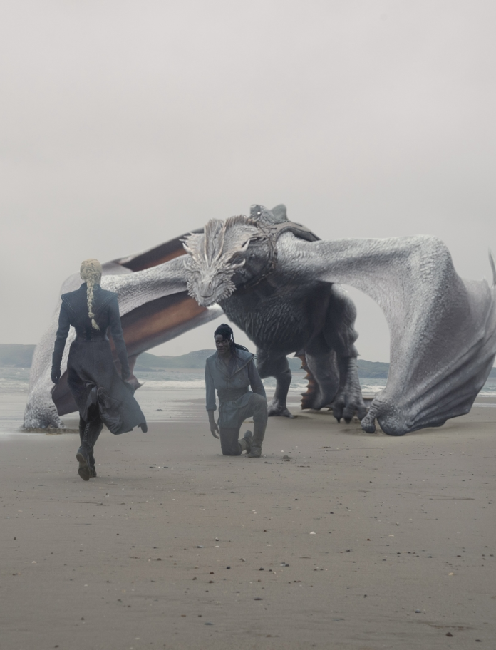 A large white dragon on a sandy beach with two people on the sand.