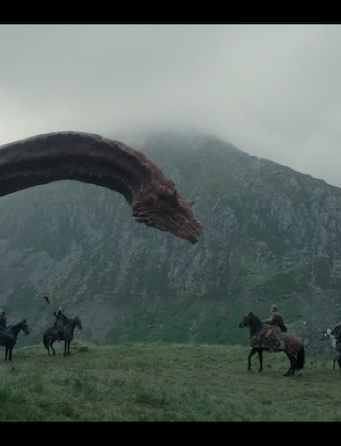 A large red dragon in mountainous countryside overlooking armed people on horseback.