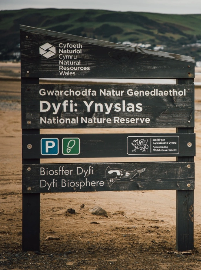 Nature reserve signpost on a sandy beach with town in the distance behind.