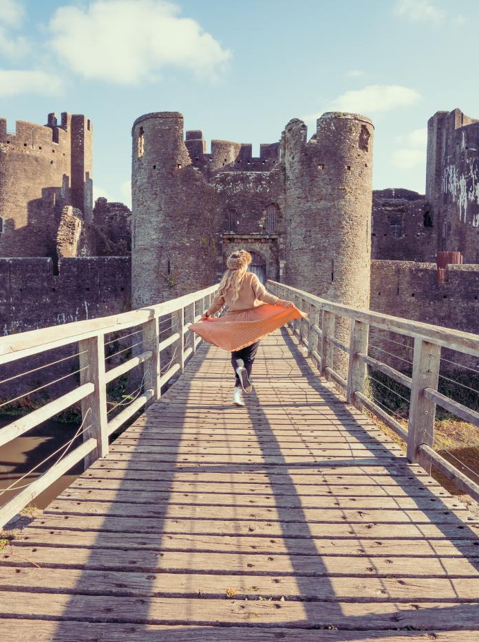 A woman dances across a drawbridge towards a large castle