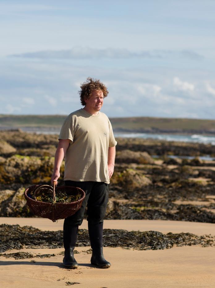 Forager Matt Powell standing on a beach holding a basket